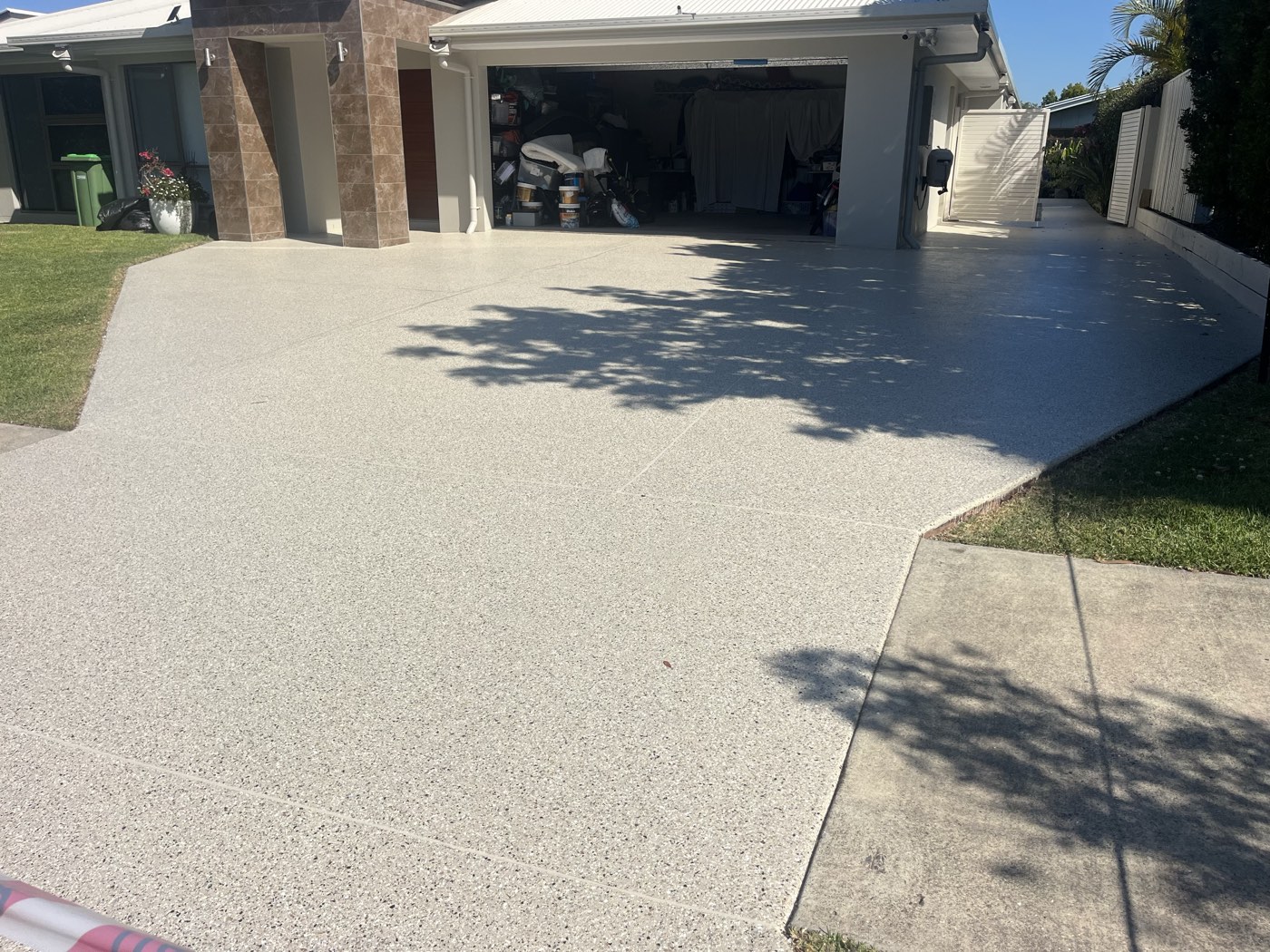 The same driveway after coating, a light grey and white flake finish running from the open garage down to the grass verge and footpath.